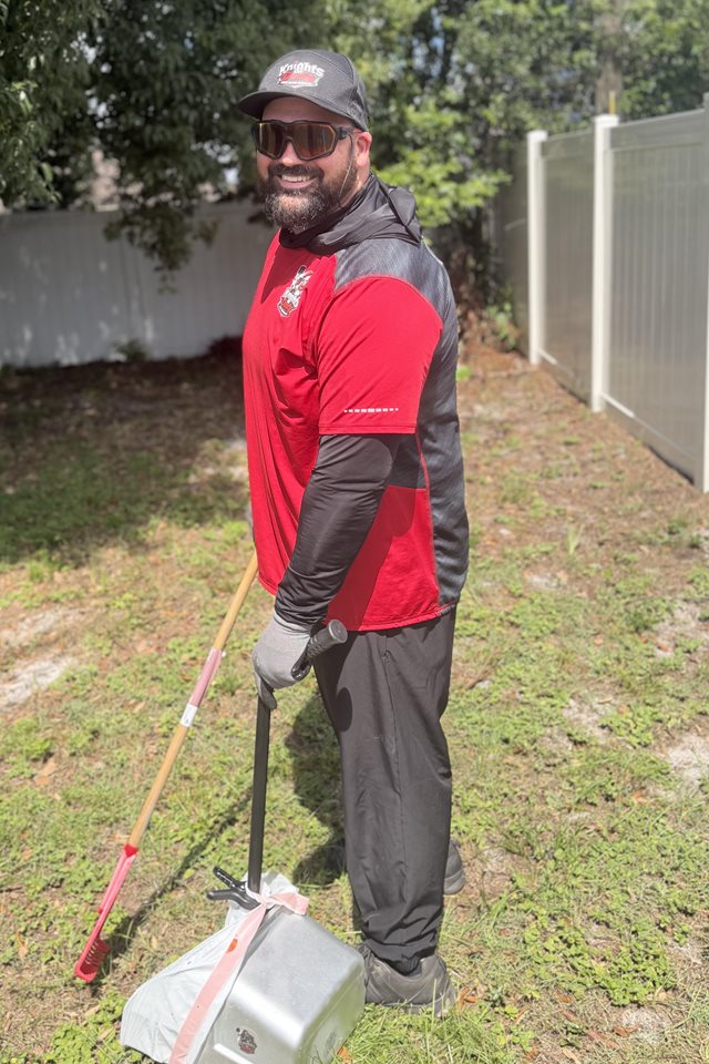 Josh from Knights On Dooty in a customer's backyard with a rake and pooper scooper